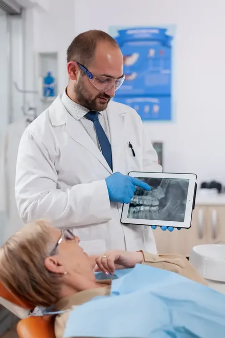 Zahnarzt erklärt einer Patientin ihre Röntgenaufnahme auf dem Tablet
